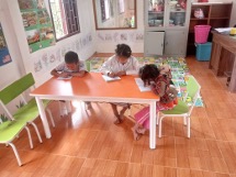 Three children writing at a desk in a classroom