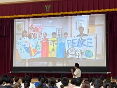 Children watching a screen showing children holding colourful banners with the word Peace